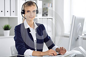 Modern business woman or confident female accountant in headset in office communicating with desktop pc. Student girl