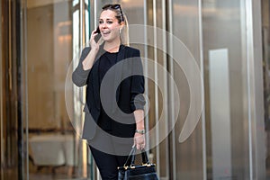 Modern business woman entrepreneur, wealthy and successful CEO outside office building, walking and talking on cellphone