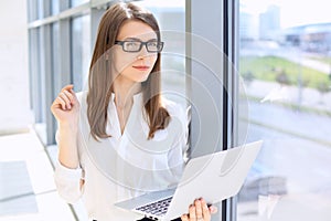 Modern business woman typing on laptop computer while standing in the office before meeting or presentation