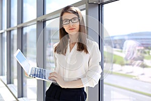 Modern business woman typing on laptop computer while standing in the office before meeting or presentation