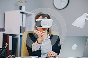 Modern business woman wearing virtual reality glasses in office. Young girl using VR goggles in office. Pretty woman