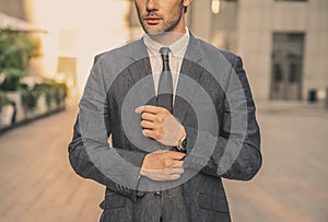 Modern businessman. Confident young man in full suit adjusting his sleeve and looking away while standing outdoors with cityscape