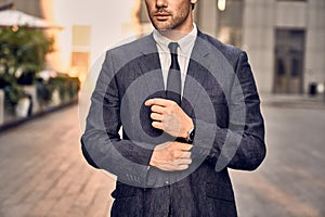 Modern businessman. Confident young man in full suit adjusting his sleeve and looking away while standing outdoors with cityscape