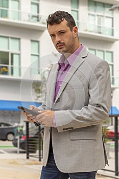 A modern businessman looks at the camera with a stern expression holding a smartphone