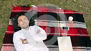 Modern businessman and relaxing with hands behind head on the grass with laptop near by