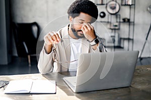 A modern businessman rubs his eyes in fatigue or exasperation while working on his laptop