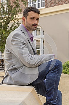 A modern businessman sits outdoors with a relaxed expression