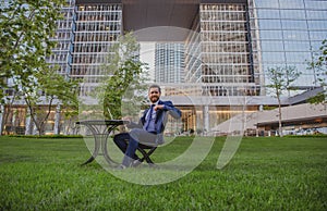 Modern businessman using gadget on coffee break. Business man working at desk in park near office building.