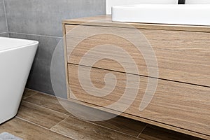 A modern cabinet hanging on the washbasin in the bathroom with a matte black faucet, the floor is covered with ceramic tiles imita