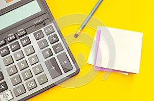 Modern calculator and pencil with stickers for notes on a yellow background, top view