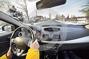 Modern car interior with driver female hands on steering wheel, winter snowy landscape outside. Safe driving concept