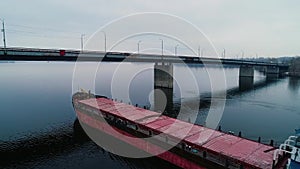 Modern cargo ship going under the bridge on the wide river