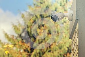 Modern CCTV camera on building wall, foliage background