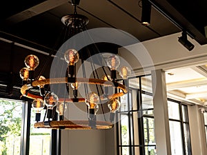 Modern chandelier in living room near glass window, loft style, vintage ceiling light or light bulbs hanging from wooden ceiling.