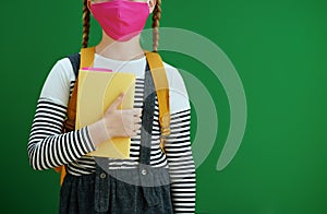 Modern child with backpack, textbook and mask isolated on green