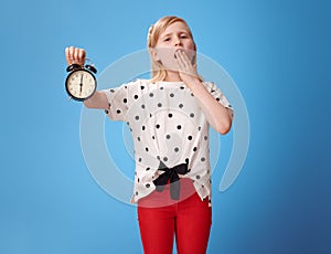 Modern child showing alarm clock and yawing on blue photo