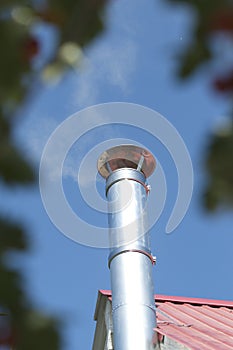 Modern chimney on the roof of house. Clean metal chimney pipe on the blue sky background.