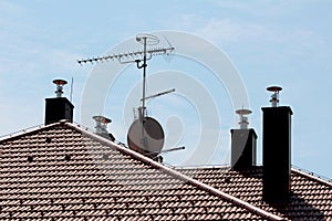 Modern chimneys with new shiny metal pipes on top surrounding tall metal pole with multiple TV antennas on top of family house