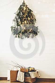 Modern christmas eco tree of pine branches hanging on wall with festive lights and presents in rustic basket. Stylish christmas