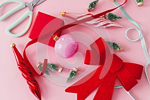 Modern Christmas flat lay. Stylish red bow, baubles, little green trees, ribbons and gift on pink background. Creative pink