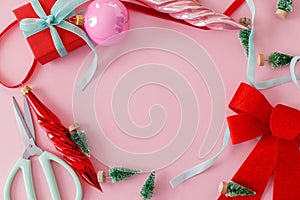 Modern Christmas flat lay. Stylish red bow, baubles, little green trees and ribbons on pink background. Creative christmas