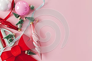 Modern Christmas flat lay. Stylish red bow, baubles, little green trees and ribbons on pink background. Creative christmas