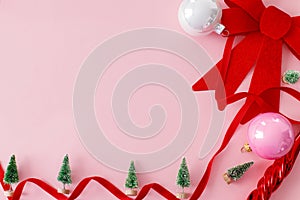 Modern Christmas flat lay. Stylish red bow, baubles, little green trees and ribbons on pink background. Creative christmas