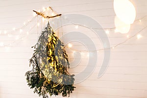 Modern christmas tree made of pine branches with golden festive lights hanging on white wooden wall. Alternative eco christmas