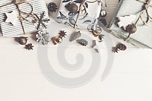 modern christmas wrapped presents with ornaments and cones on white wooden background top view, space text. merry christmas