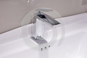 Modern chrome faucet on a white bathroom sink. The faucet design is a modern combination of geometric shapes and smooth