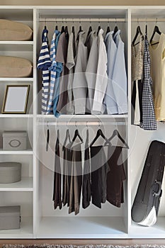 Modern closet with row of cloths hanging in white wardrobe