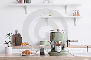 Modern coffee machine, jar of beans and croissant on counter in kitchen