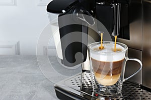 Modern coffee machine making latte into glass cup on grey table, closeup. Space for text