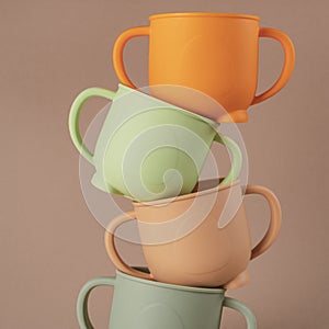 Modern colorful pastel silicone cups stacked in column on brown background. Baby tableware, first feeding.