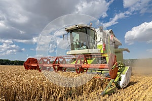 Modern combine harvester  harvesting on wheat field, cloudy sky