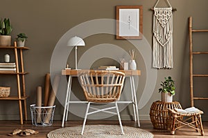 Modern composition at boho interior of home office room with wooden desk, stylish armchair, bamboo shelf, carpet, macrame.