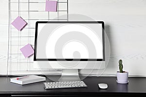 Modern computer monitor on desk against light wall,