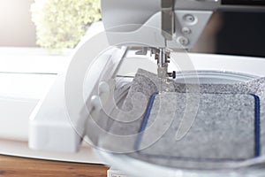 modern computerised sewing machine with embroidery unit stitching a blue frame on grey felt in a friendly work environment