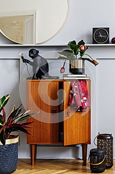 Modern concept of home staging with design wooden commode, round mirror, shelf, clock, plant, rattan decor, book, lanterns.