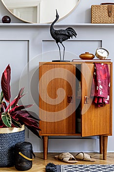 Modern concept of home staging with design wooden commode, round mirror, shelf, clock, plant, rattan decor, book, lanterns.