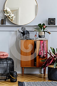 Modern concept of home staging with design wooden commode, round mirror, shelf, clock, plant, rattan pouf, carpet, books.