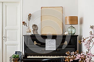 Modern concept of mock up poster frame with design black piano, table lamp, gold clock, dried flowers in vase.