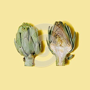 Modern concept of two fresh organic artichoke halves lies down against light yellow  background. Flat lay composition