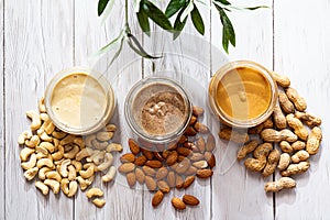 The modern concept of wellness and veganism. Jars of almond, cashew and peanut butter on a white wooden table with an olive branch