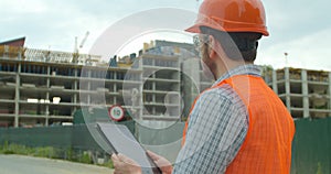 Modern construction engineer or architect in helmet at construction site works with industrial electronic tablet. Close