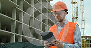 Modern construction engineer or architect in helmet at construction site works with industrial electronic tablet. Close