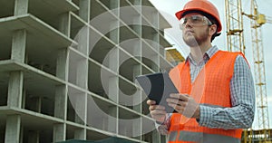 Modern construction engineer or architect in helmet at construction site works with industrial electronic tablet. Close