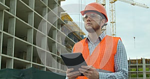 Modern construction engineer or architect in helmet at construction site works with industrial electronic tablet. Close