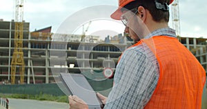 Modern construction engineer or architect in helmet at construction site works with industrial electronic tablet. Close