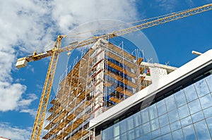 Modern construction finishing the facade of the house with glass window panels, scaffolding crane
